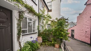 Une rue étroite, avec une maison blanche sur la gauche, une maison rose sur la droite et un portail noir.