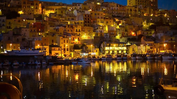 A coastal town at night with buildings reflecting on the water, a dock with boats, and a prominent building with a balcony. - [European Apartment] Town Center + Self Check-in (Catania)