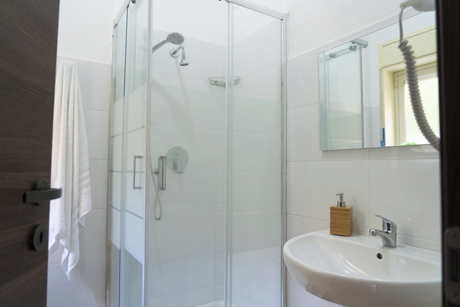 Une salle de bain moderne avec une douche à parois de verre, un lavabo blanc et un distributeur de savon en bois.