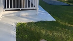 Ein weißes Gebäude mit einer Veranda und einem Rasen.