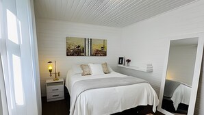 Ein Schlafzimmer mit Bett, Nachttisch, Lampe, einem Gemälde, einem Spiegel und einem Teppich.