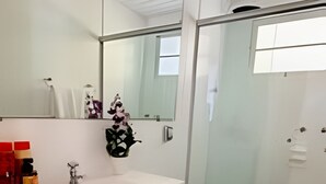 Ein modernes Badezimmer mit einem weißen Waschtisch, einer Duschkabine aus Glas und einem großen Spiegel.