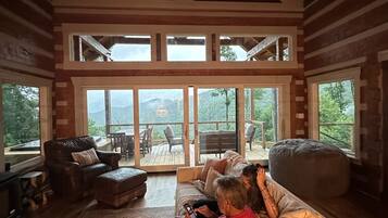 A spacious living room with a high ceiling, large windows, and a view of the outdoors.