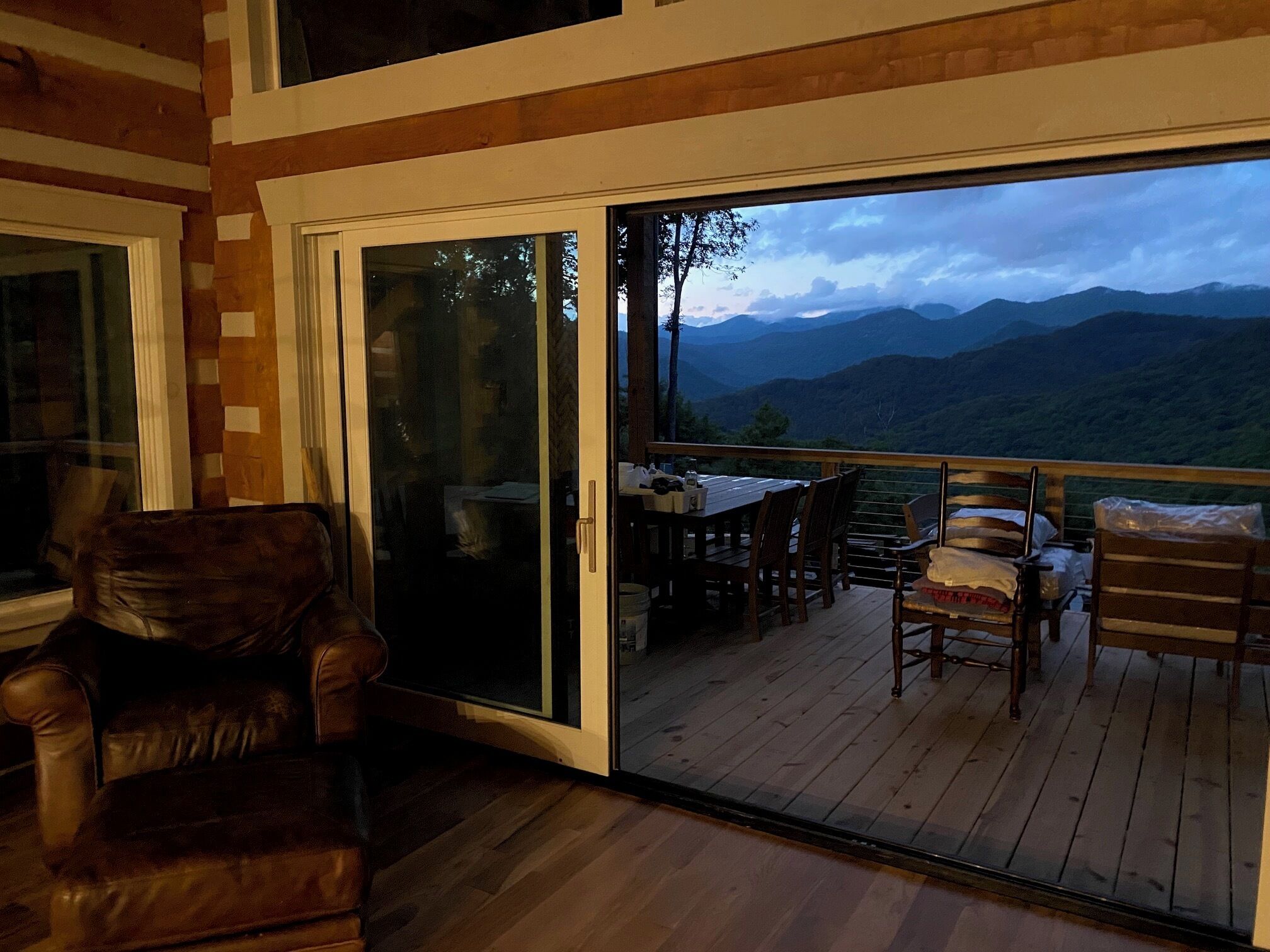 A wooden deck with a table and chairs, a sliding glass door leading to a mountain view.