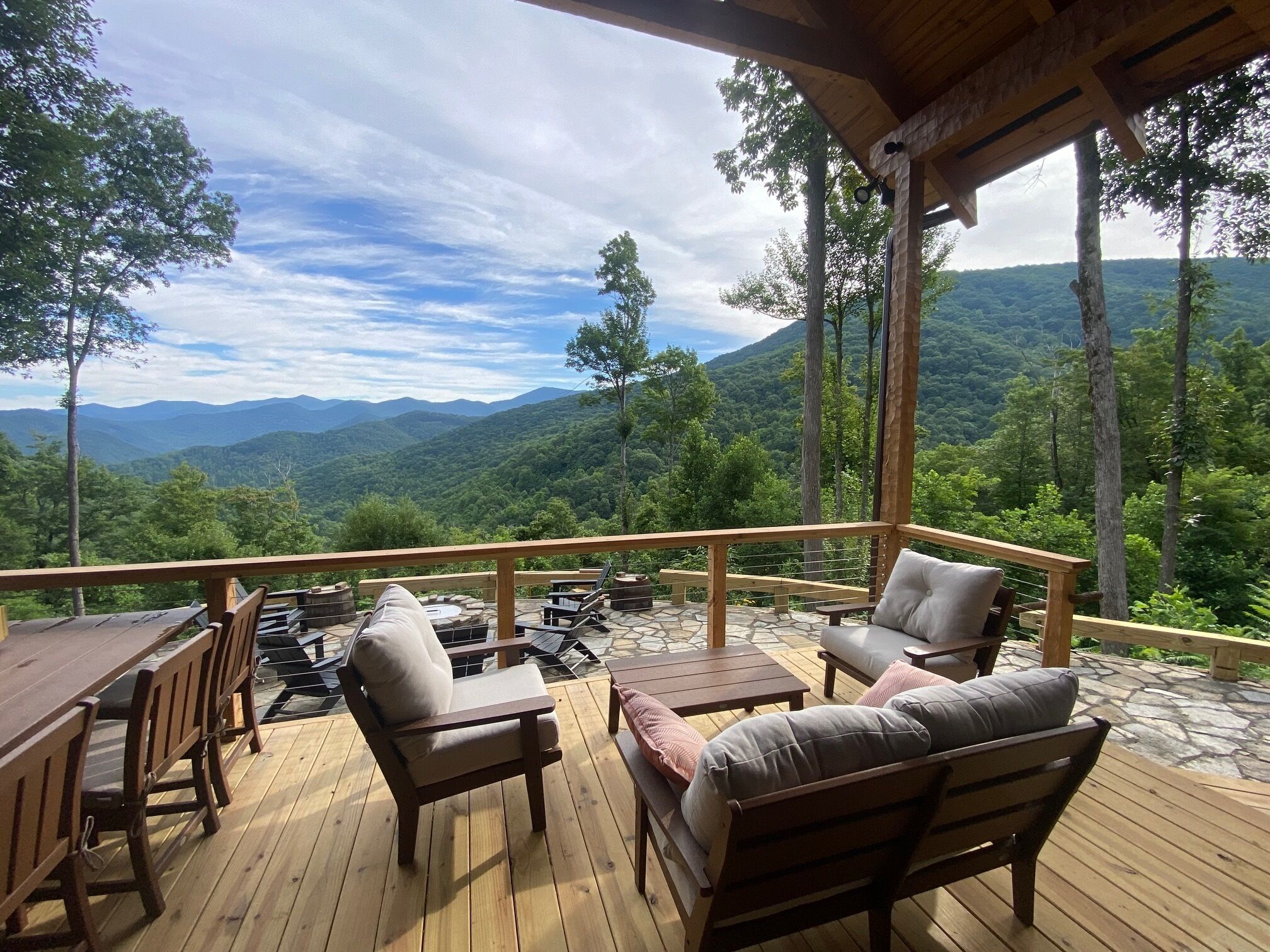 Une terrasse en bois, aménagée avec du mobilier d’extérieur, notamment une table et des chaises, qui offre une vue sur un paysage montagneux.