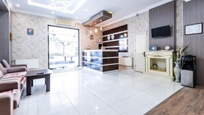 A modern hotel lobby with a reception desk, seating area, and a television.