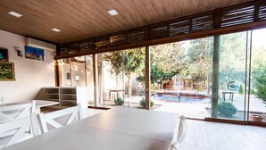 A modern interior with a large dining area, a view of the outdoor swimming pool, and a wooden ceiling.