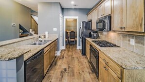A modern kitchen with wooden cabinets, granite countertops, a stainless steel refrigerator, and a built-in oven.