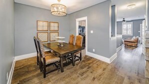 A dining area with a wooden table and chairs, a chandelier, and framed artwork on the wall.