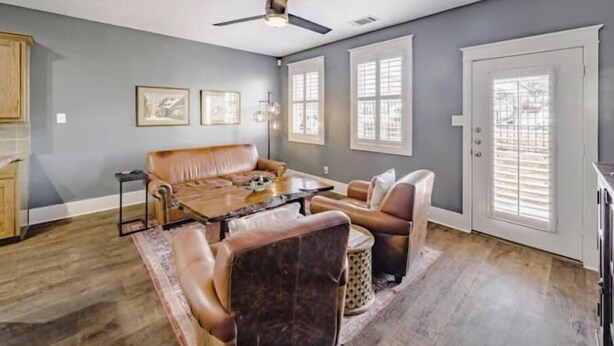 A spacious living room with a brown leather sofa, a coffee table, and a ceiling fan.