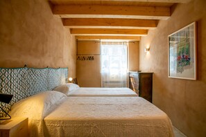 A bedroom with two beds, wooden beams on the ceiling, a nightstand, a dresser, and a framed picture on the wall.