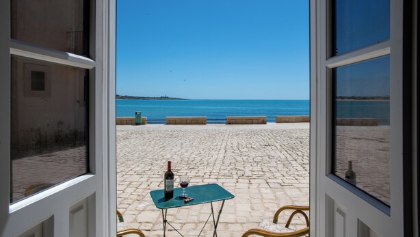 A view from a window to a cobblestone patio with a table, a bottle, and a glass of wine. - House with direct sea access in Sampieri with 3 bedrooms (Sampieri)