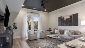 A modern living room with a grey sofa, two armchairs, a coffee table, and a TV on a stand. - 2 Bedroom, Main Level- ADA Accessible (Helena)