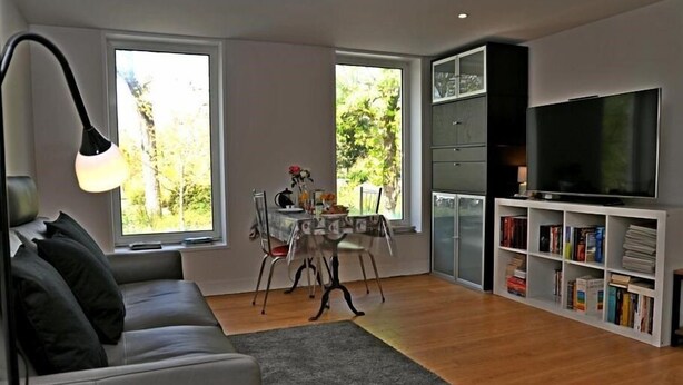 Un salon moderne avec un canapé gris, une table à manger avec des chaises, une bibliothèque et un téléviseur.