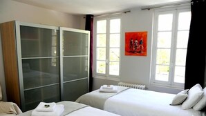 Une chambre d’hôtel avec deux lits, une armoire et une fenêtre ornée d’un tableau.