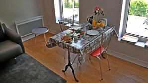 Un coin repas avec une table mise pour le petit-déjeuner, un canapé gris et une fenêtre donnant sur un paysage verdoyant.