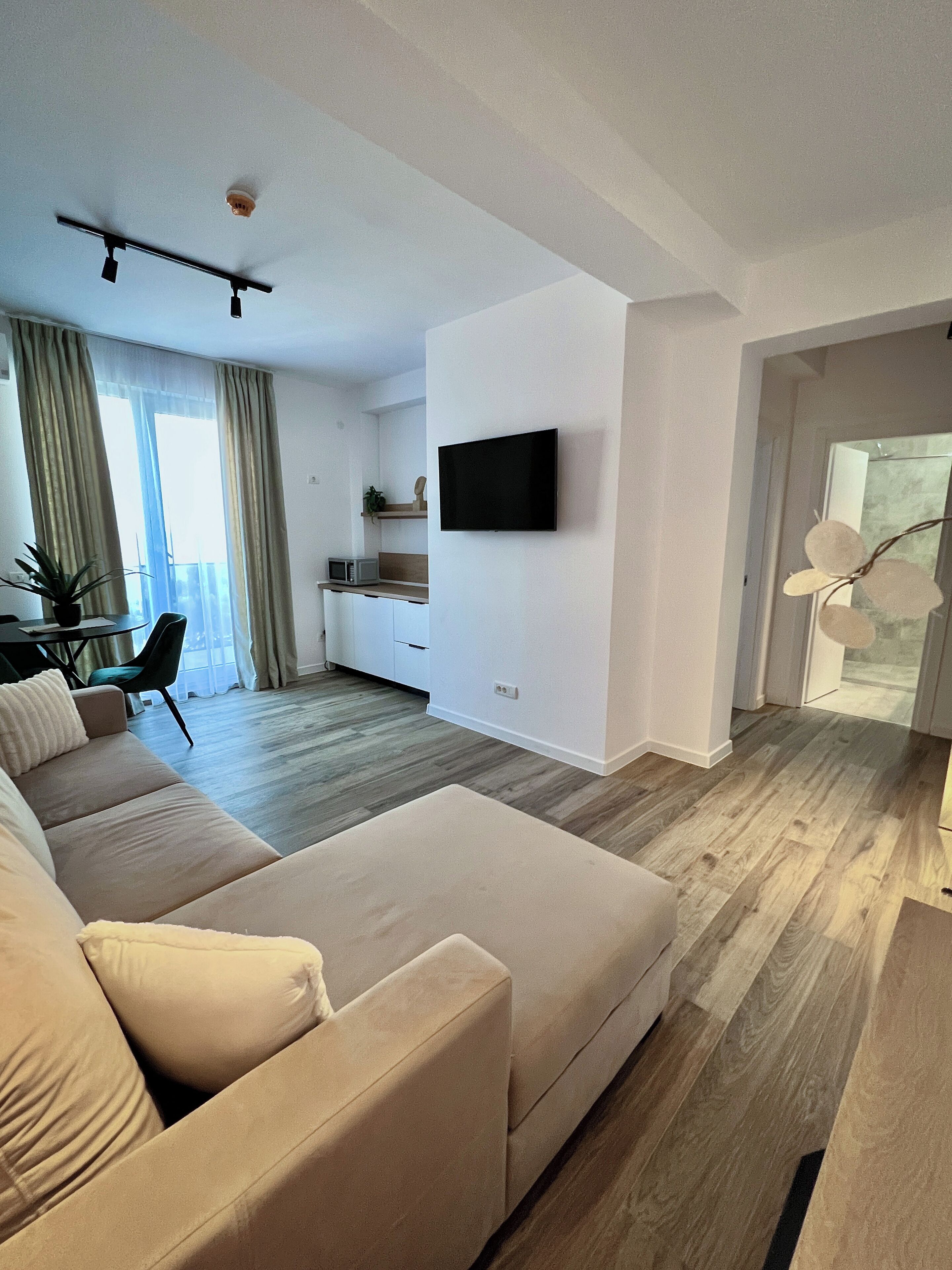 A modern living room with a sofa, a flat-screen TV mounted on the wall, and a dining area with a table and chairs.