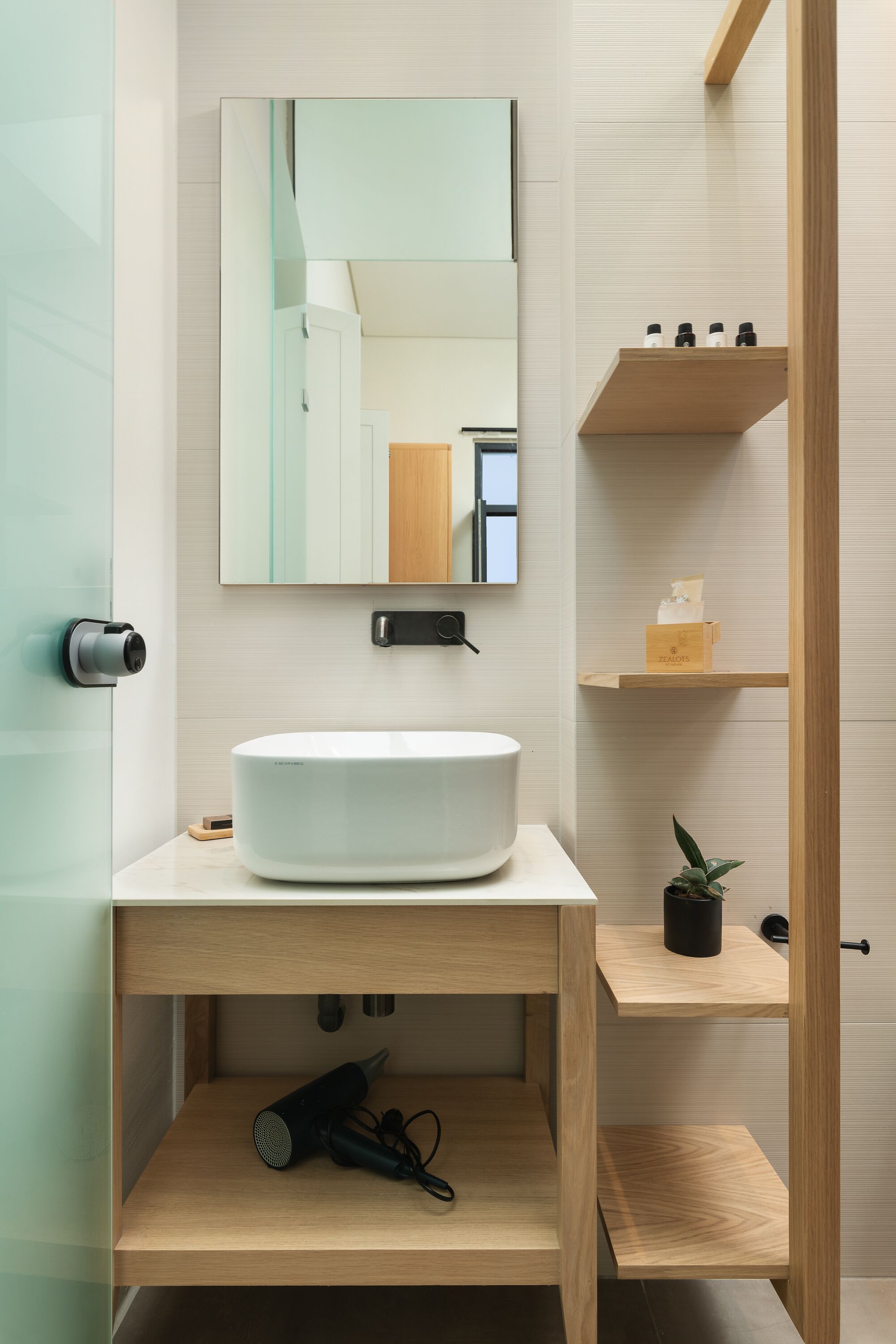 A modern bathroom with a white sink, a mirror, and wooden shelves.