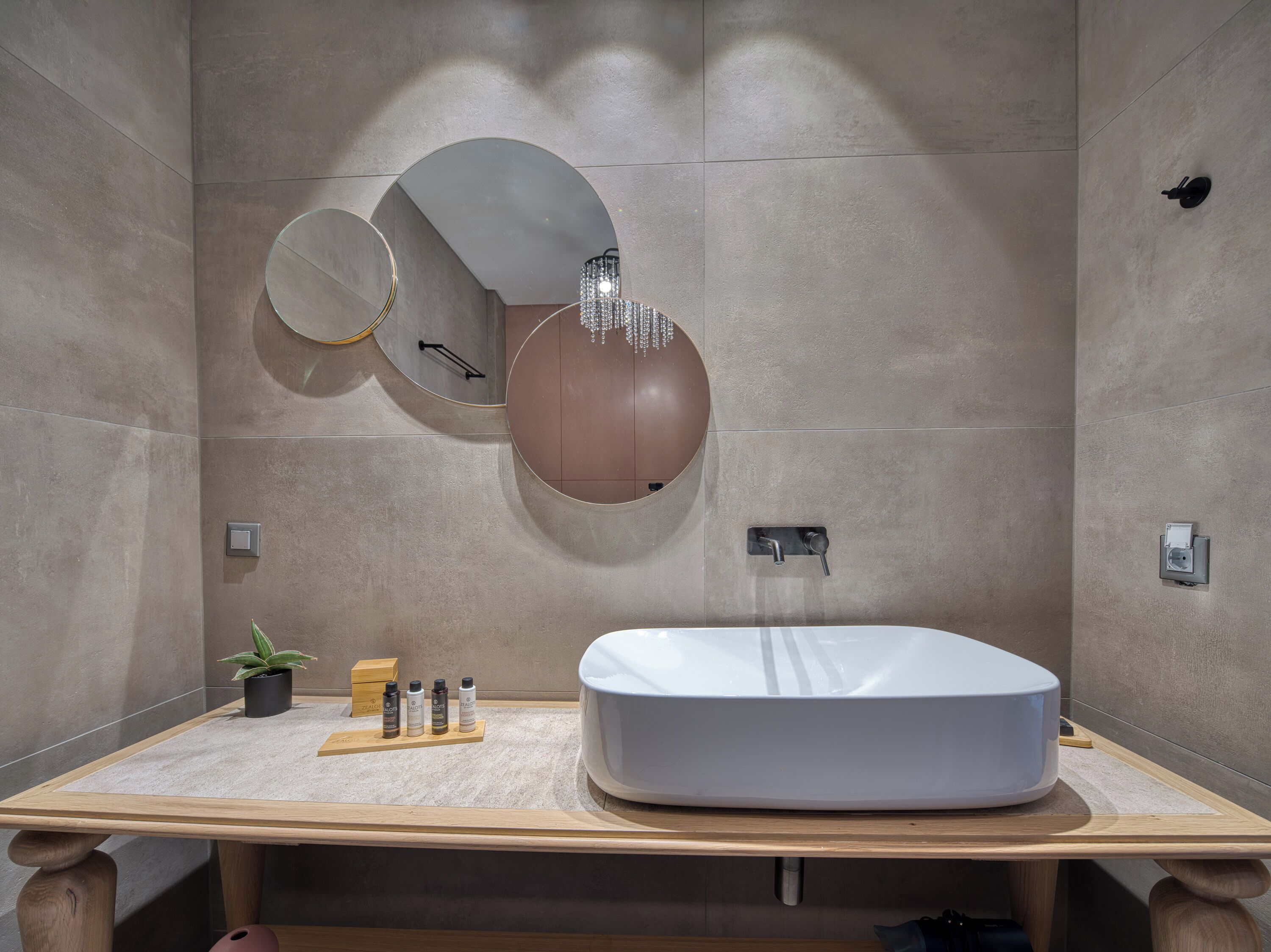 Un baño moderno con un lavamanos ovalado grande, un espejo redondo y una lámpara de pared.
