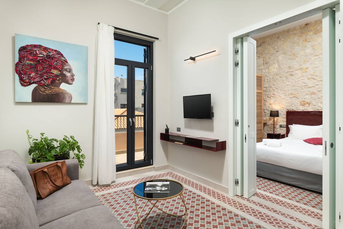 Een moderne hotelkamer met een grijze bank, een bijzettafeltje, een schilderij, een televisie, een bed en een stenen muur.