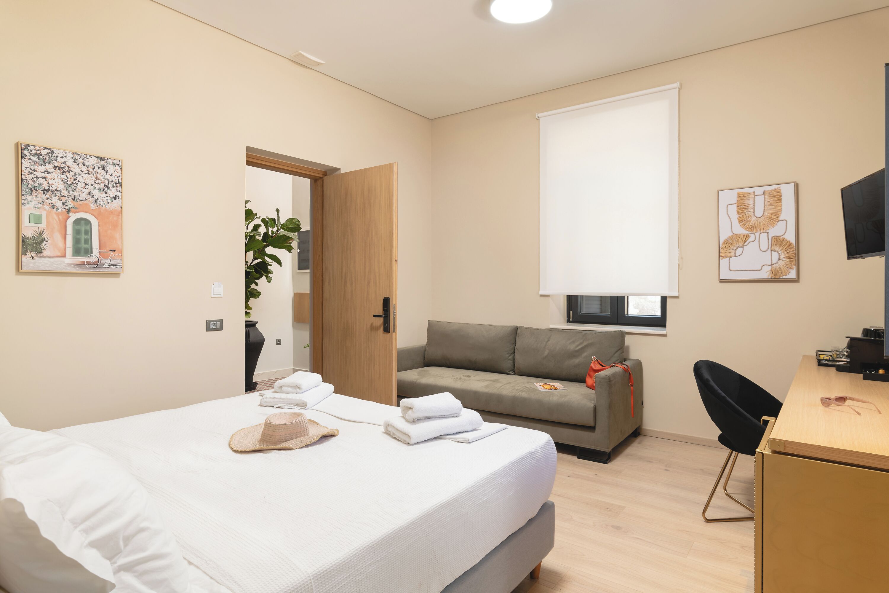 A modern hotel room with a bed, a sofa, a desk, and a TV.