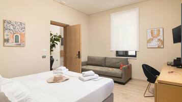 A modern hotel room with a bed, a sofa, a desk, and a TV.