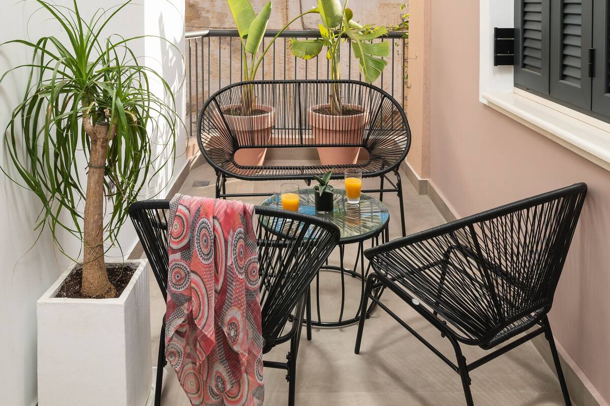 Een balkon met een bloempot, twee stoelen, een tafeltje met een glas sinaasappelsap, en uitzicht op de skyline.