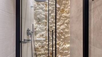 Una ducha moderna con puerta de cristal, pared de piedra y diseño minimalista.