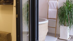 Une salle de bain moderne avec une porte en verre, un lavabo rond, un porte-serviettes et une plante en pot.