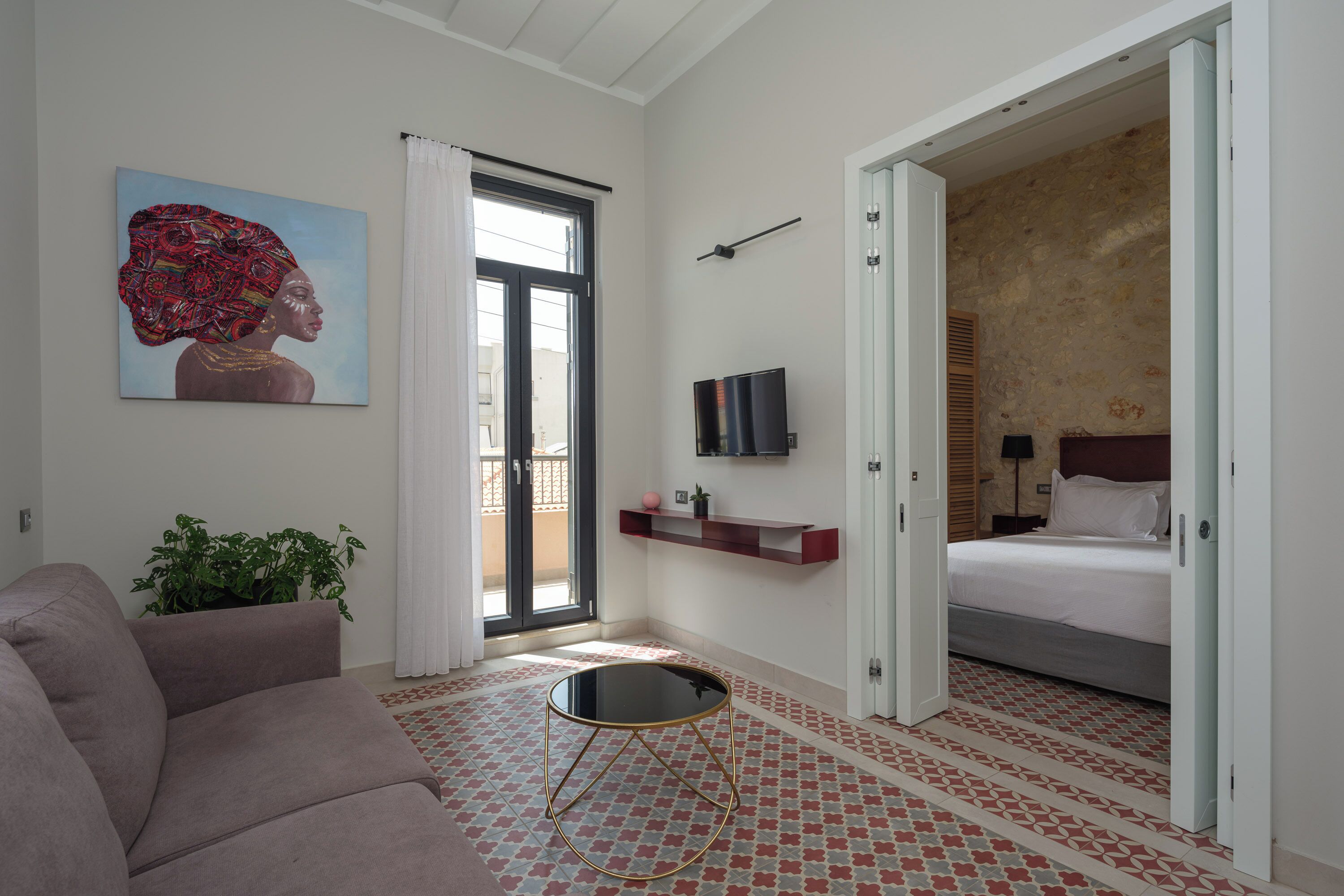 Une chambre d’hôtel moderne équipée d’un canapé, d’une petite table ronde, d’un téléviseur, d’un lit et d’une grande fenêtre avec des rideaux.