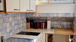 Eine kompakte Küche mit weißen Schränken, einer Edelstahl-Spüle und einem eingebauten Backofen. Ein Fenster über der Spüle bietet Blick ins Freie.