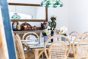 Een eetgedeelte met rieten stoelen, een glazen tafel en een spiegel erboven.