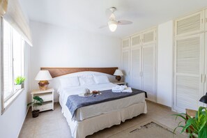 Een keurig opgemaakt slaapkamer met een bed, nachtlampjes, een plafondventilator en een raam met een plant.