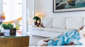 Ein Wohnzimmer mit einem weißen Sofa, einem Gemälde von Booten an der Wand, einer Lampe und einer Pflanze auf der Fensterbank.