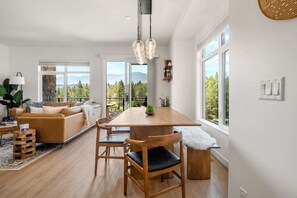 Un salon moderne avec une table à manger en bois, un canapé en cuir et de grandes fenêtres donnant sur l’extérieur.