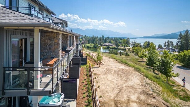 A residential property with a balcony overlooking a lake, a stone facade, and a view of mountains. - The Bauhaus | Private Hot Tub | Walk to Lake | MCM (Invermere)