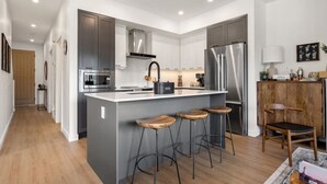 A modern kitchen with a central island, stainless steel appliances, and bar stools. - The Bauhaus | Private Hot Tub | Walk to Lake | MCM (Invermere)