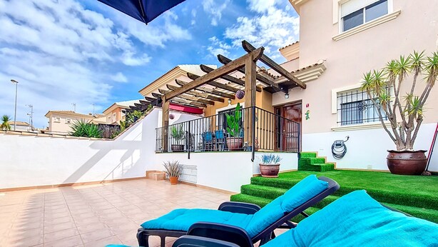 A rooftop patio with sun loungers, a pergola, and a staircase leading to a balcony.