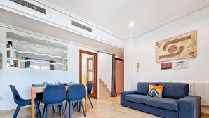 A modern living room with a dining area, featuring a sofa, chairs, and a table.