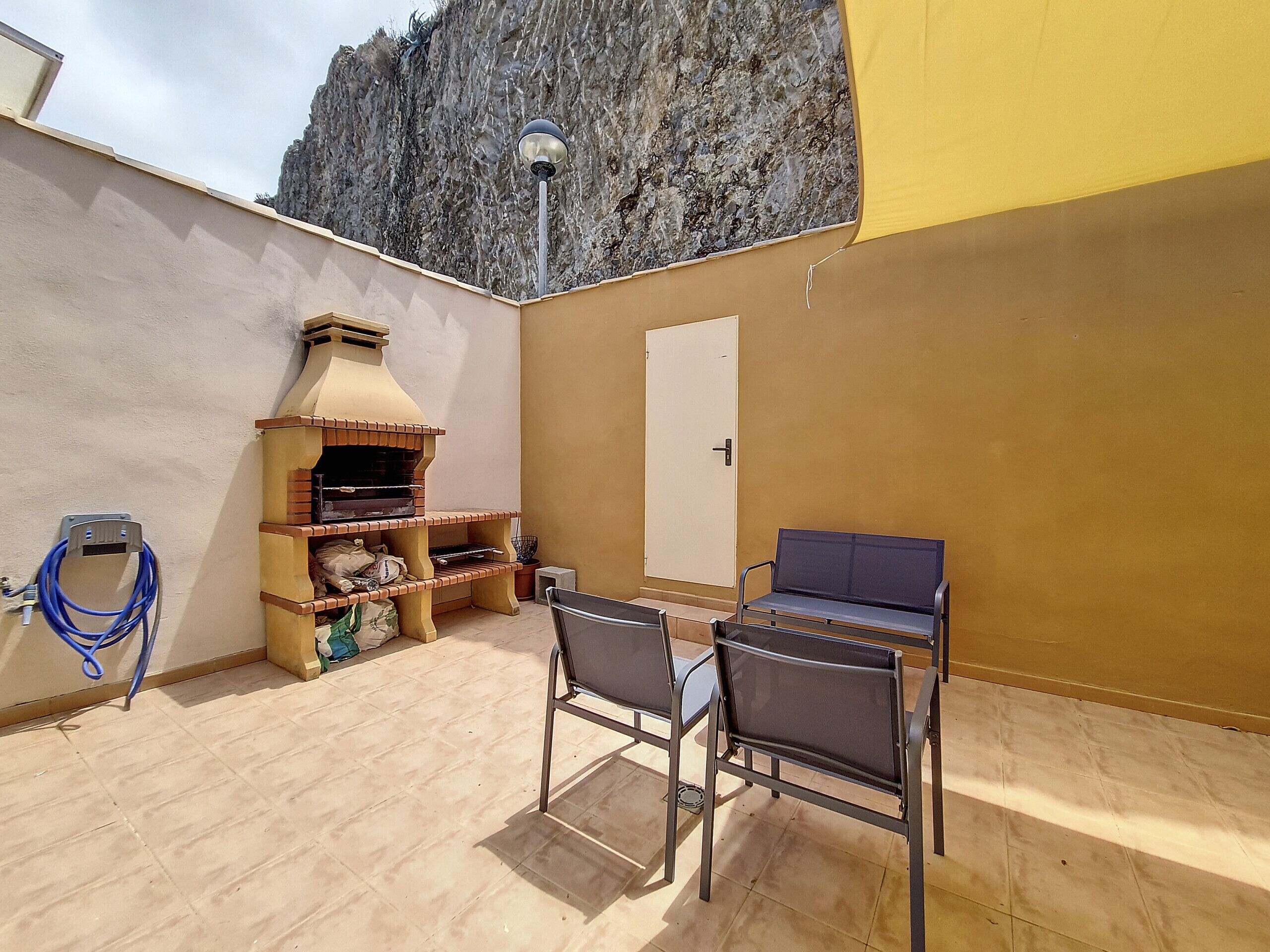 A patio with a brick oven, two chairs, a table, and a door.