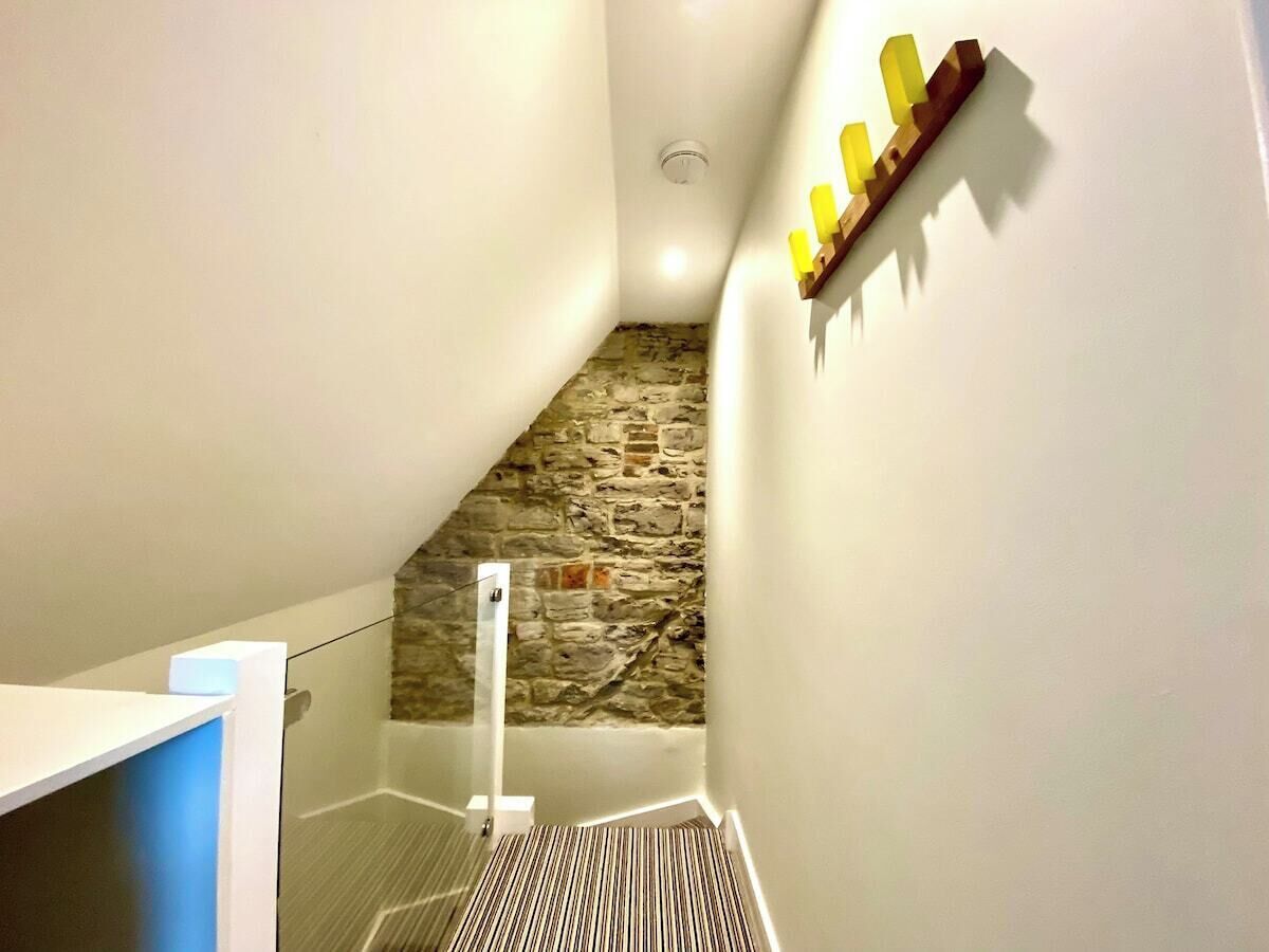 A narrow stairway with a stone wall, a white handrail, and a wooden shelf with yellow candles.