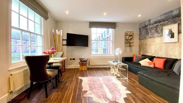 A modern living room with a wooden floor, a sofa, a TV, and a large window. - Stunning Little House on Poole Quay -Free Parking (Poole)