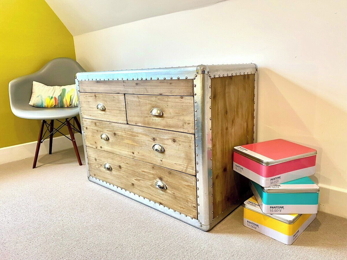 Un aparador de madera con detalles metálicos y cajones, junto a una pila de cajas Pantone de colores.