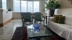 A spacious living area with a large window, a white sofa, two patterned chairs, and a glass coffee table with a blue bowl. - Ocean Front Copacabana - 1 min from the beach (Rio de Janeiro)