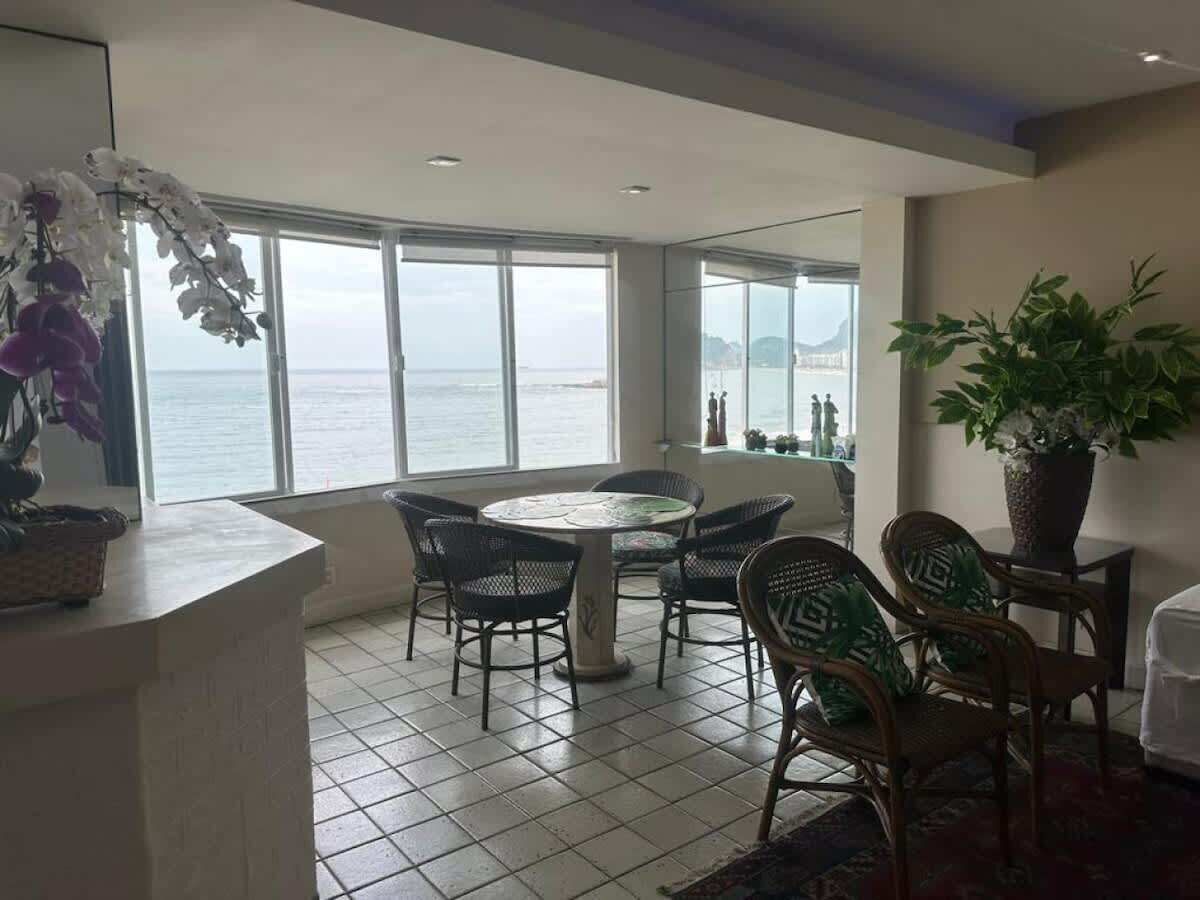 A dining area with a round table and chairs, large windows with a view of the sea, and a potted plant.
