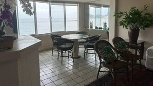 A dining area with a round table and chairs, large windows with a view of the sea, and a potted plant. - Ocean Front Copacabana - 1 min from the beach (Rio de Janeiro)