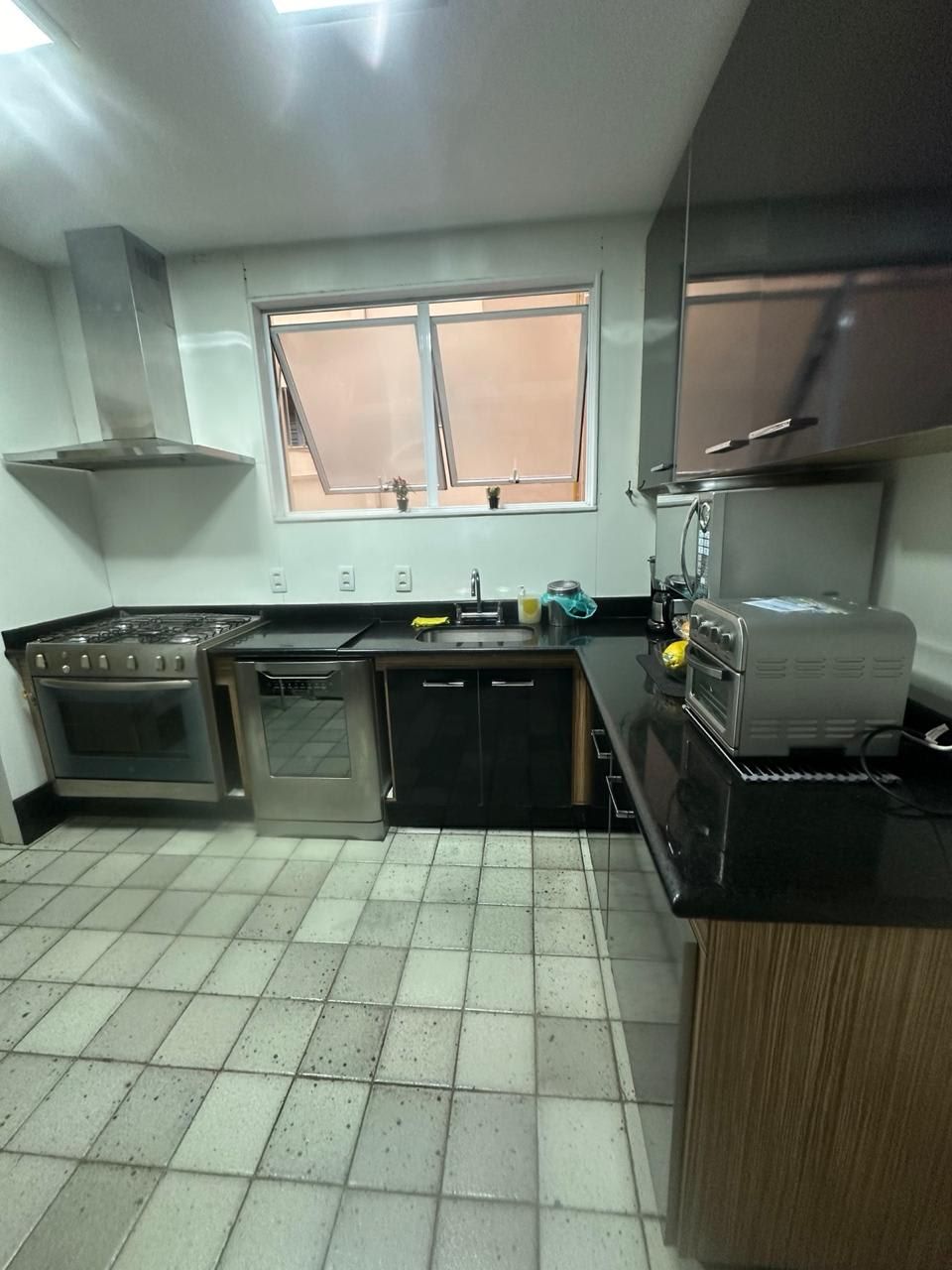Une cuisine compacte équipée d’une cuisinière à gaz, d’un four et d’un lave-vaisselle encastré. Une fenêtre se trouve au-dessus de l’évier et une hotte aspirante au-dessus de la cuisinière.