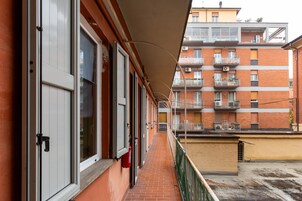 Un estrecho pasillo con suelo de ladrillo, ventanas de marco blanco y baranda verde.