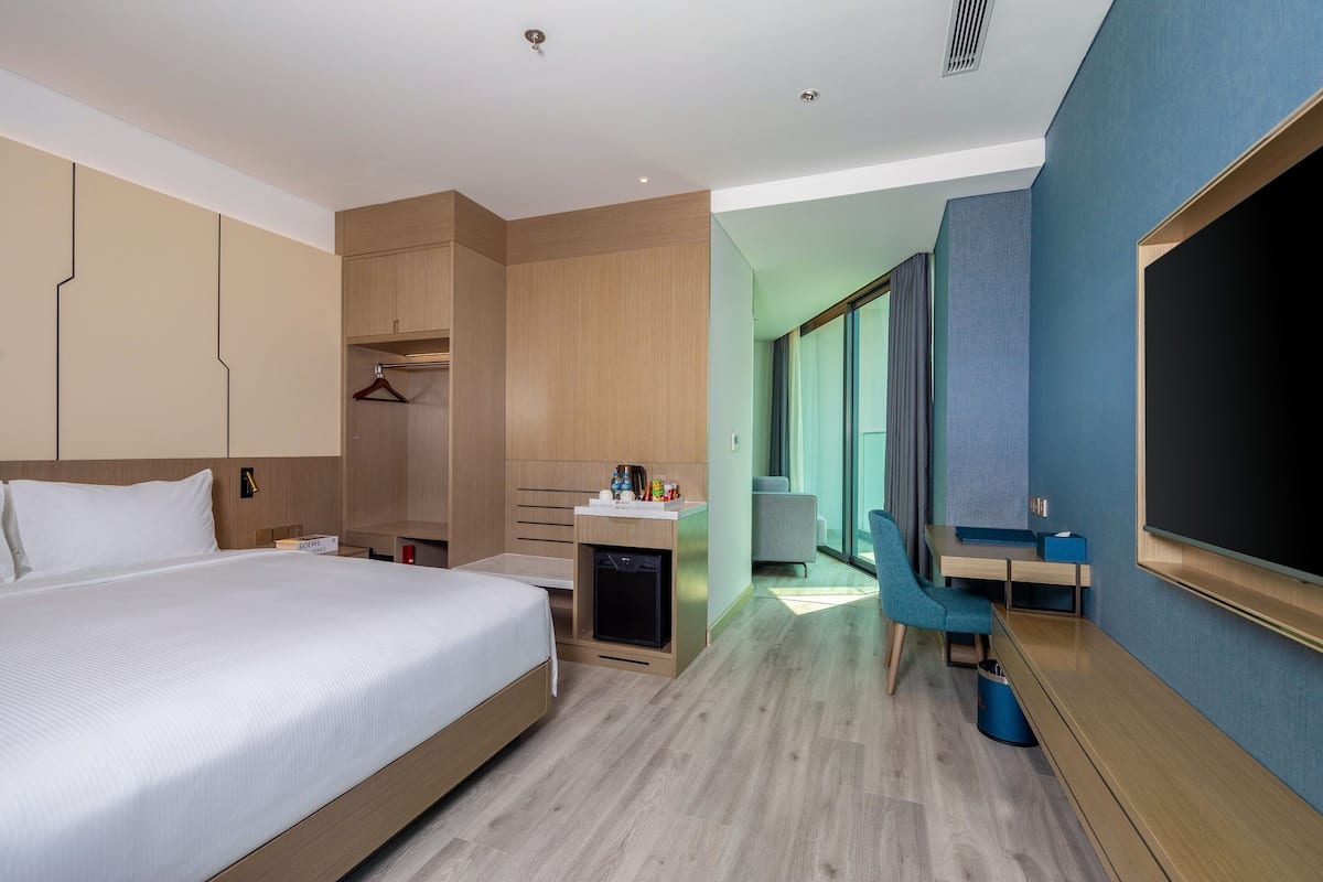 A modern hotel room with a large bed, a desk, a chair, a TV, and a wardrobe.