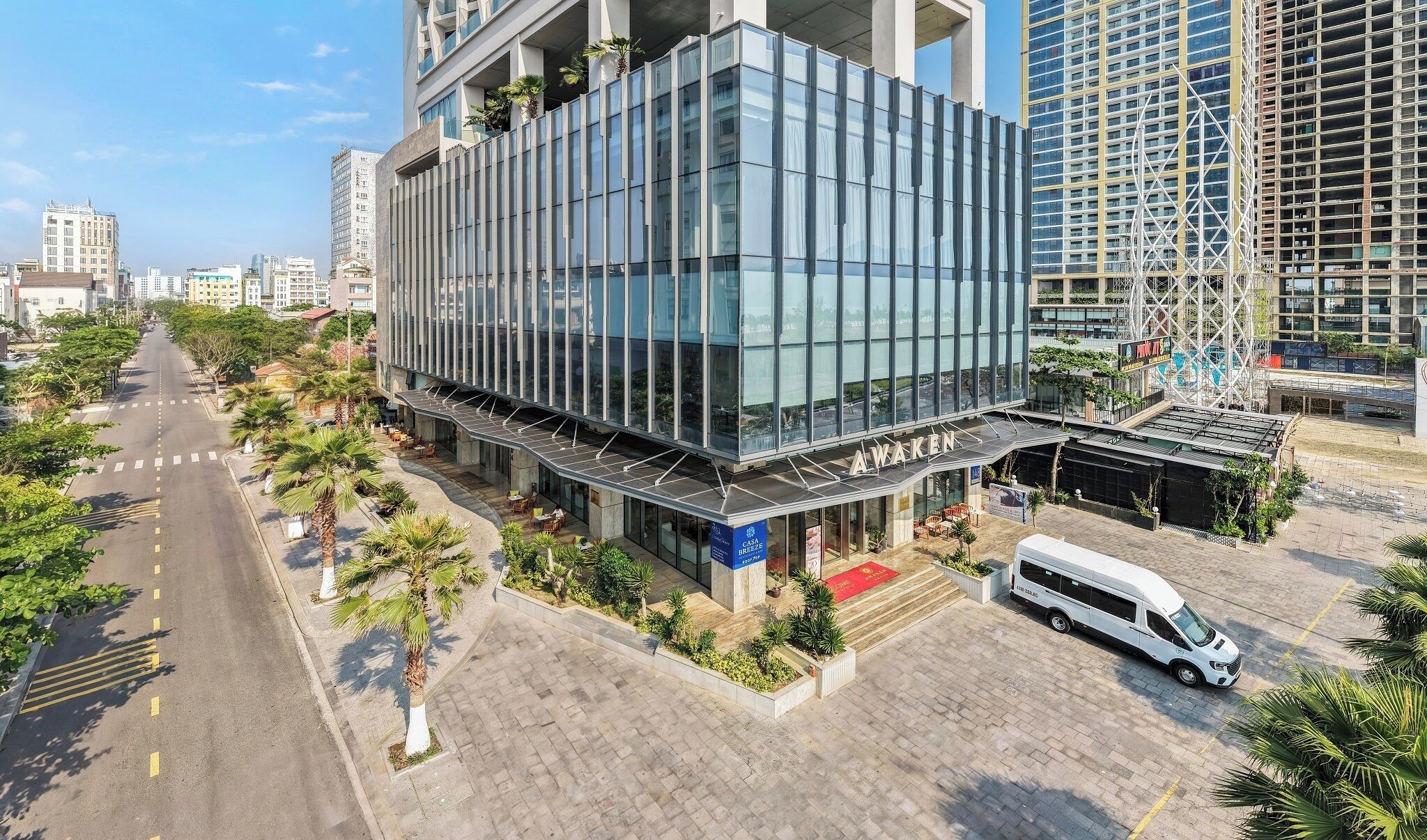 A modern building with a glass facade, a covered outdoor seating area, and a white van parked in front.